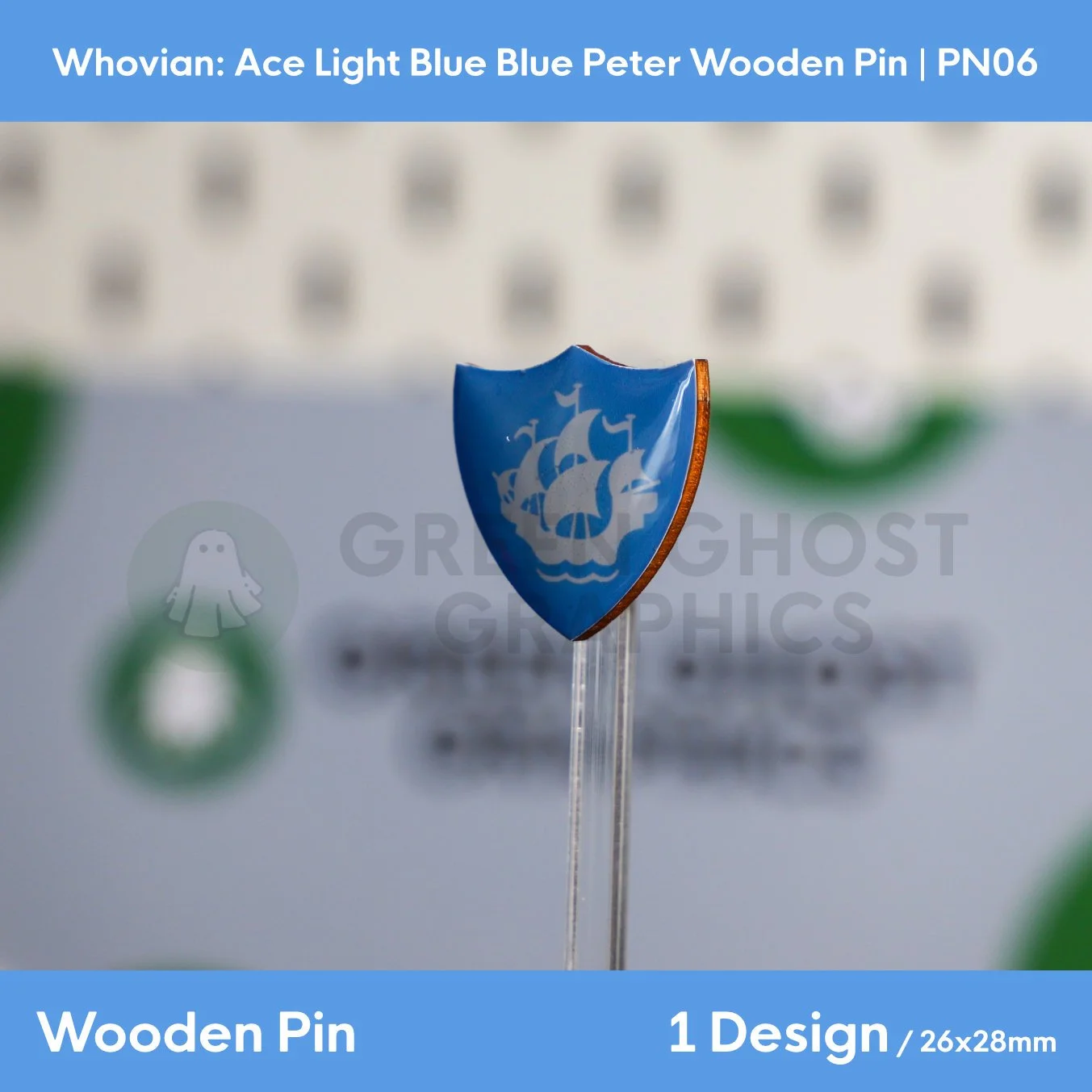 A shield‑shaped wooden pin showing a white sailing ship on a white background displayed at an angle on a transparent stand.