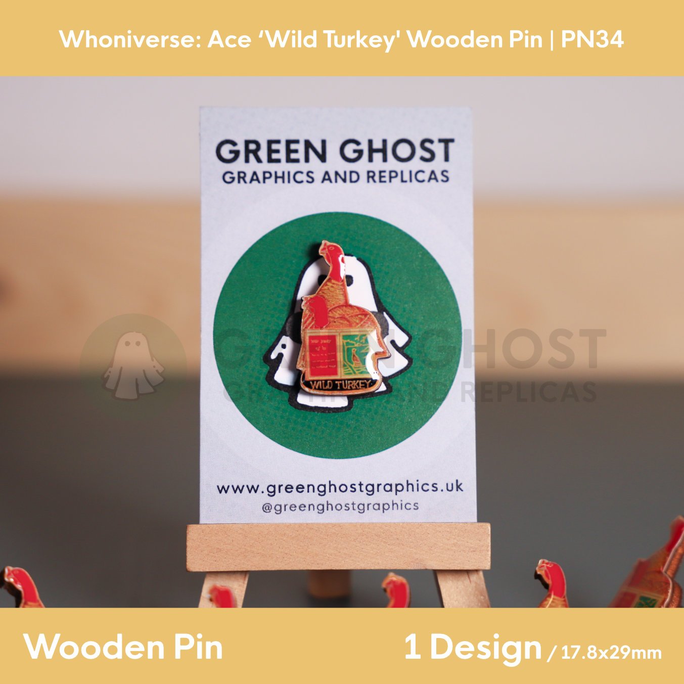 A turkey and open book wooden pin mounted on a branded backing card on a wooden easel, with multiple identical pins scattered around it on a flat surface.