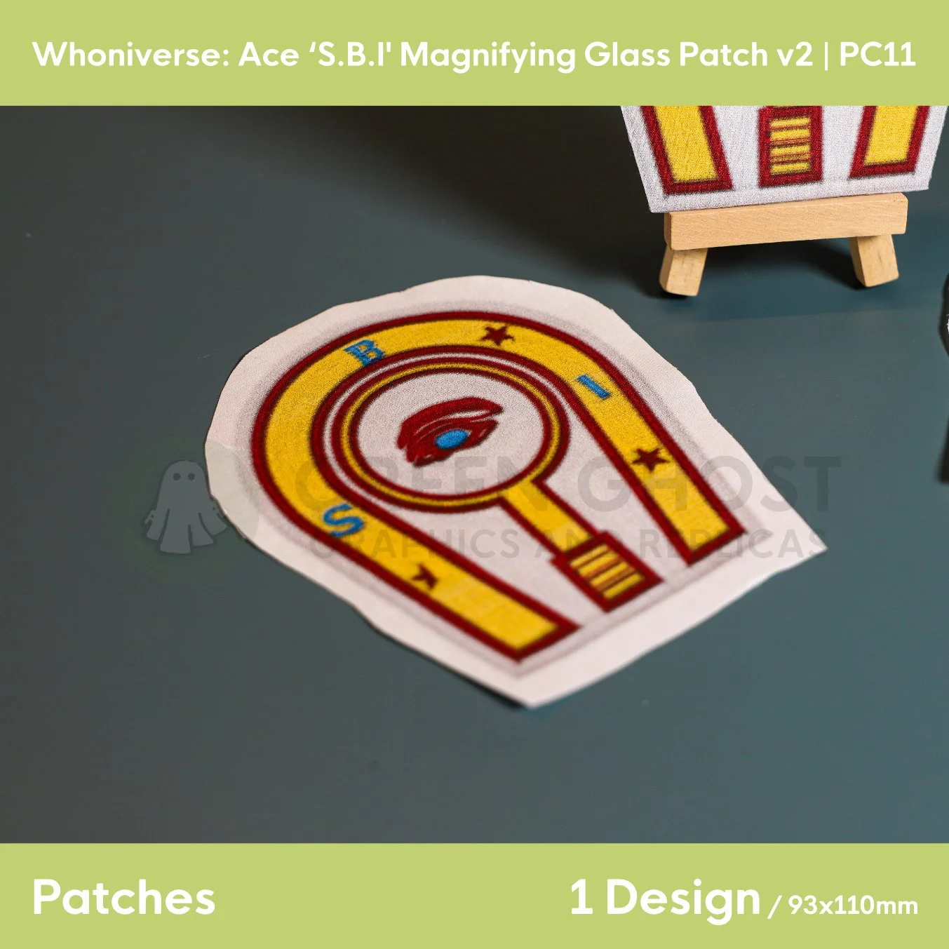 Close up of the uncut unfinished version of the magnifying glass SBI patch design, on a plain aqua green background.