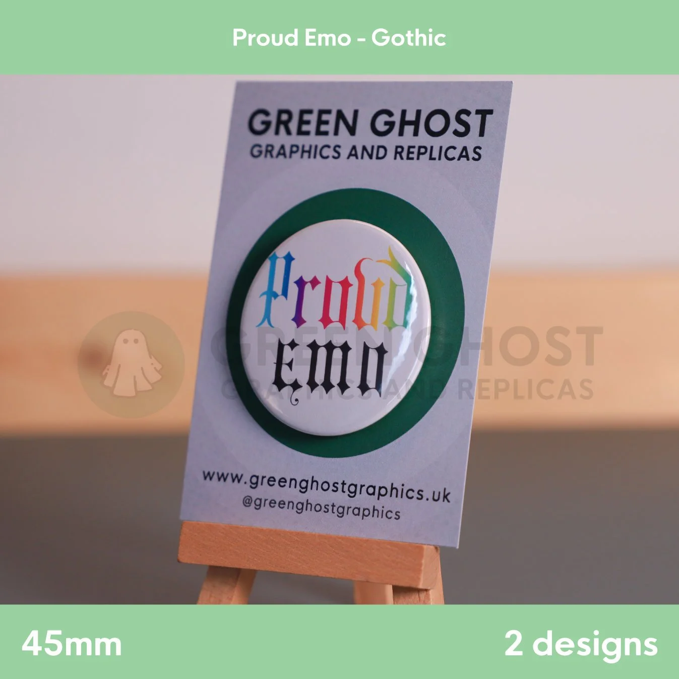 A round white badge with rainbow “Proud Emo” lettering shown on a branded card resting on a wooden easel.