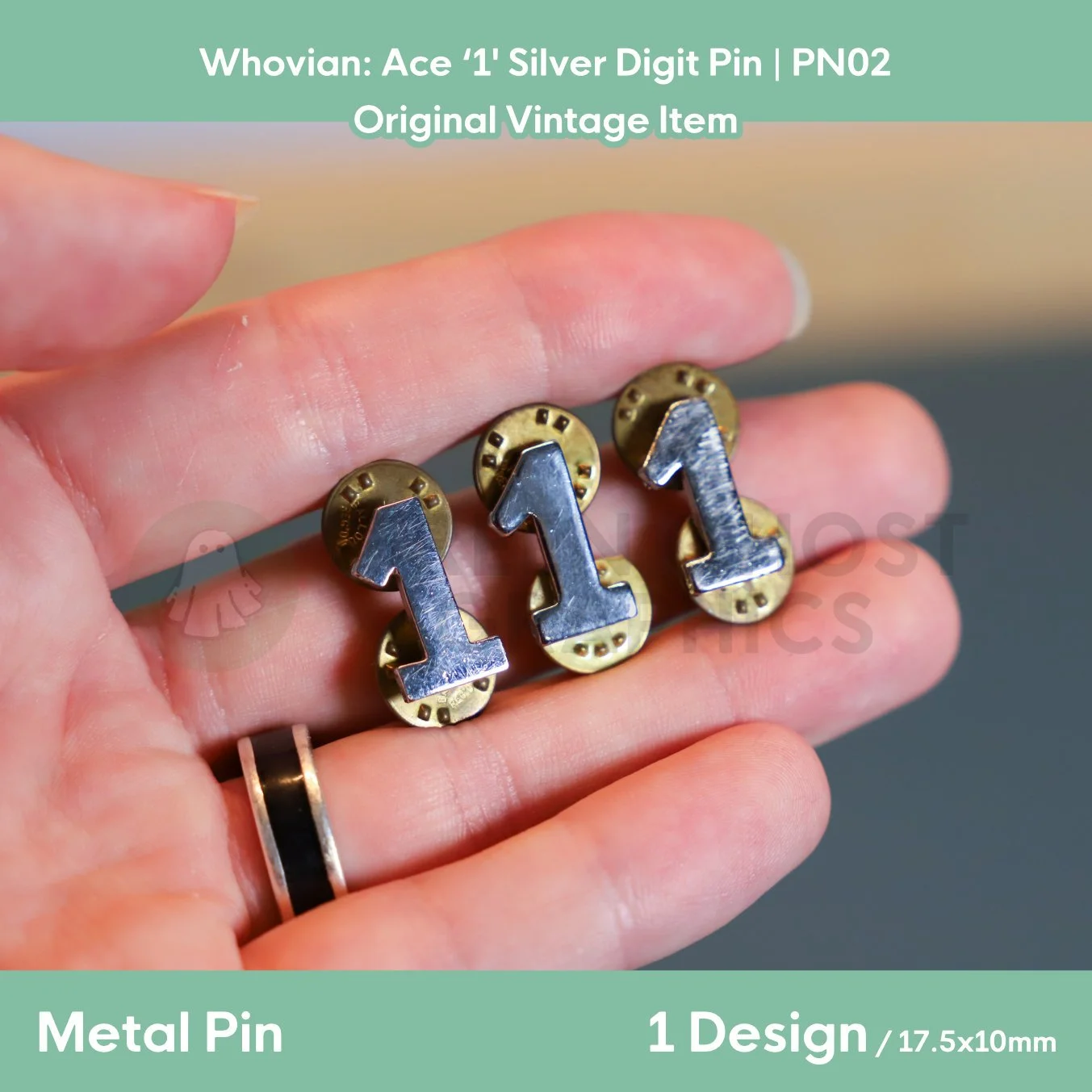 Three silver metal pins shaped like the number “1” displayed across an open hand with gold butterfly clasps visible behind them.