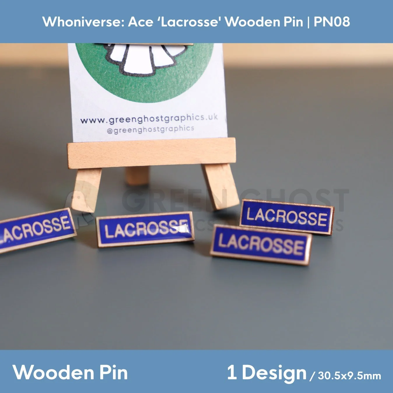 Several rectangular wooden “LACROSSE” pins with blue backgrounds and white lettering arranged on a grey surface, with one pin displayed on a branded backing card on a wooden easel.