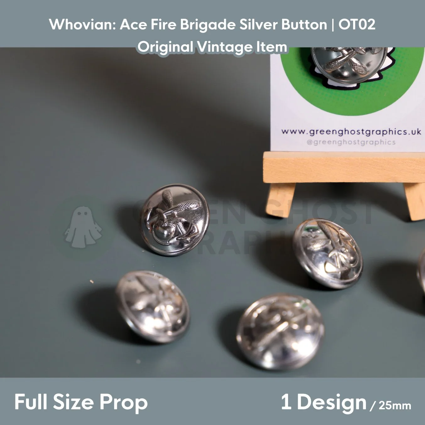 Several round silver fire brigade buttons with a raised helmet and crossed axes design displayed on a flat surface beside a wooden easel.