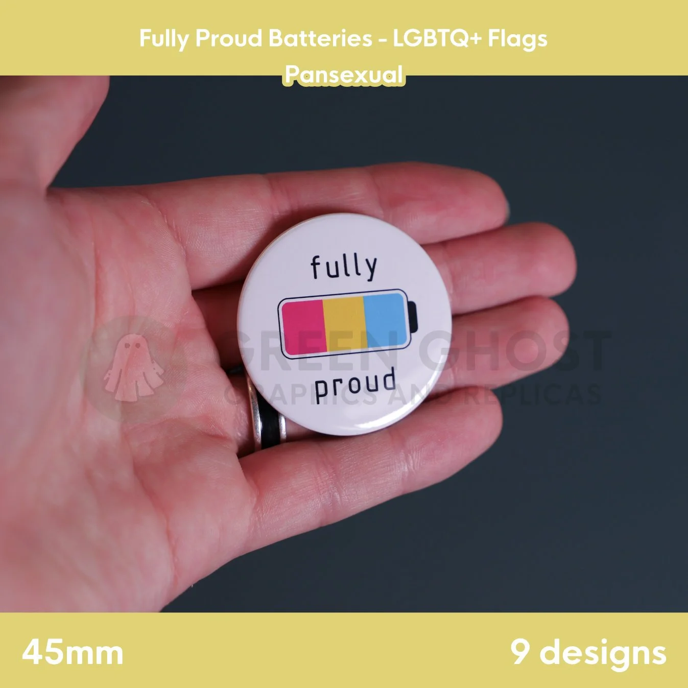 A round badge with a pink, yellow, and blue battery design held in a hand against a grey background.