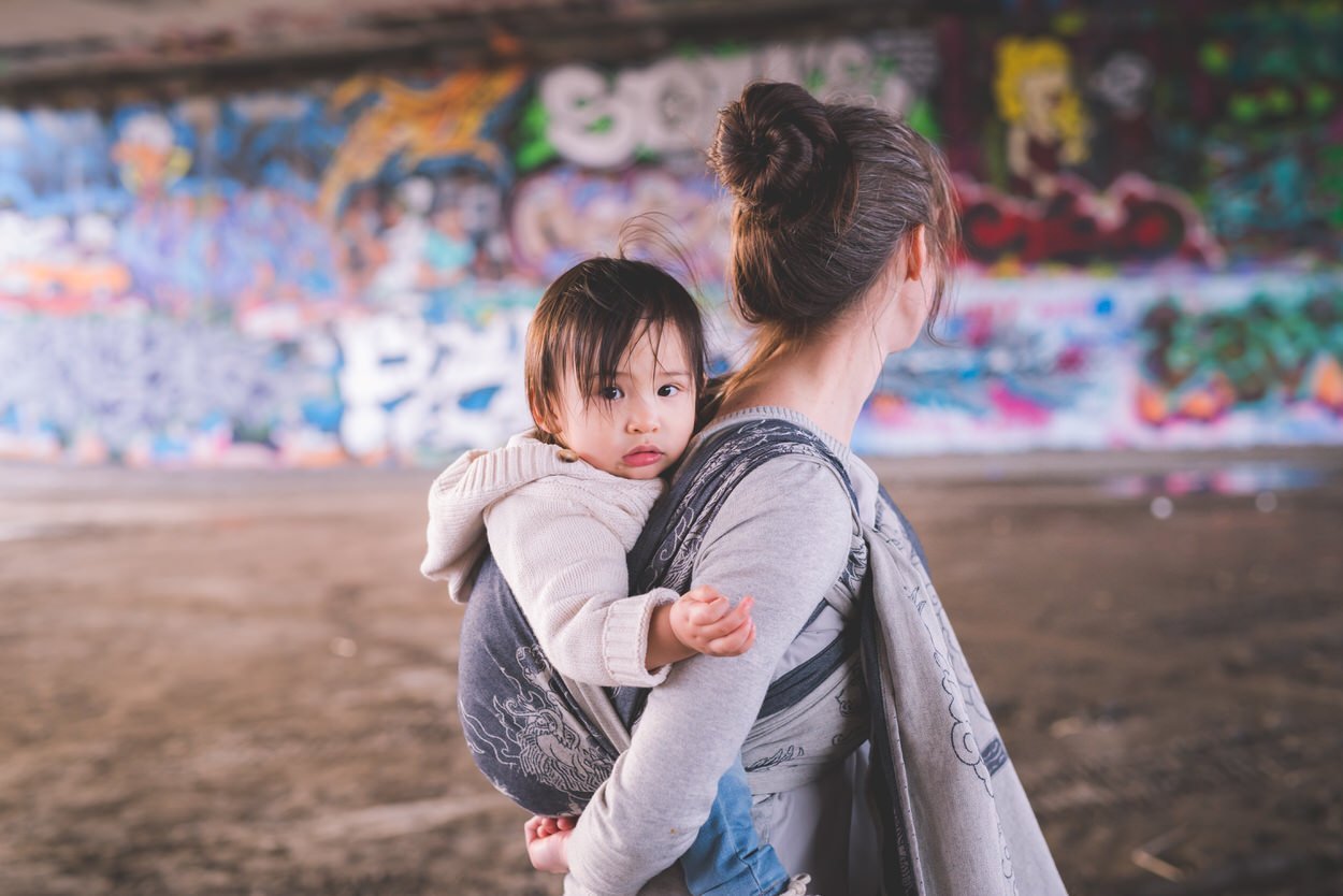 Baby on mom's back with Ottawa Grafitti Wall behind them.