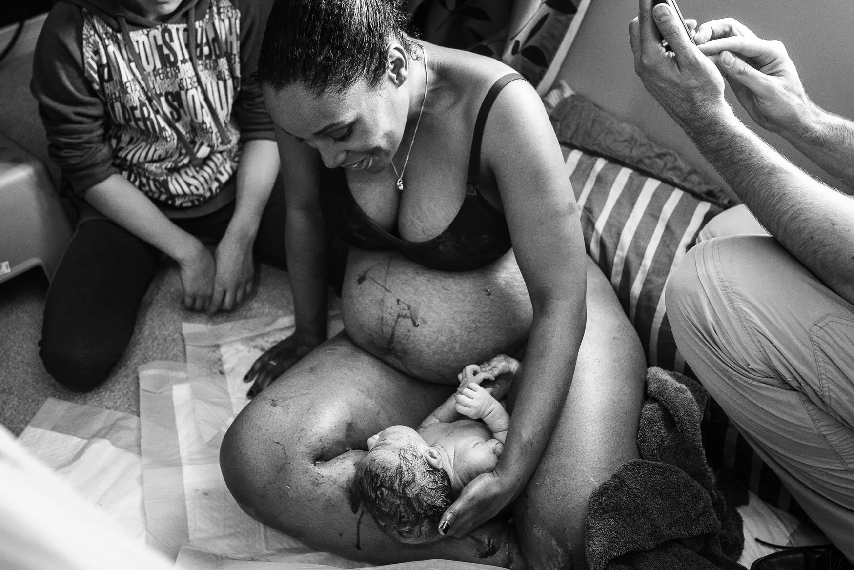 Woman holding newborn baby right after birth with window light behind her.