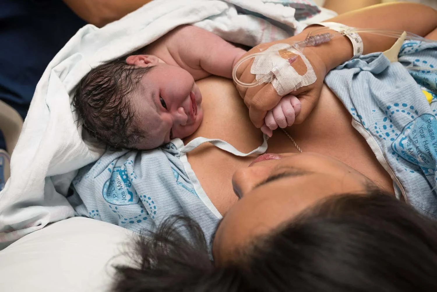 Newborn baby on mom's chest right after birth. Mom is holding his hand and he is looking right at her.
