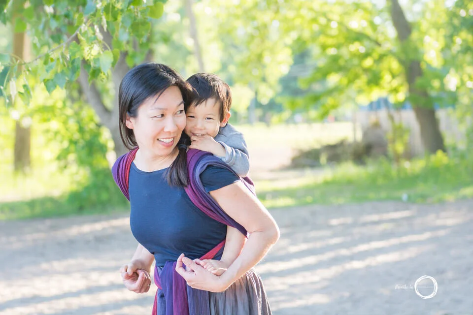Mom and son on beach smiling and laughing together in green trees as sun is setting.