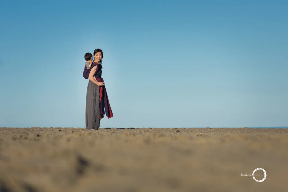 Mom and toddler son on the beach at sunset with blue sky behind them.
