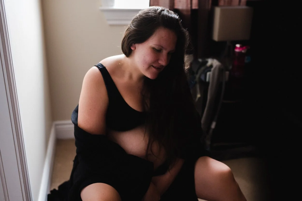 Woman sitting on a birth ball at home while in labour in very low light conditions. She looks content and peaceful.