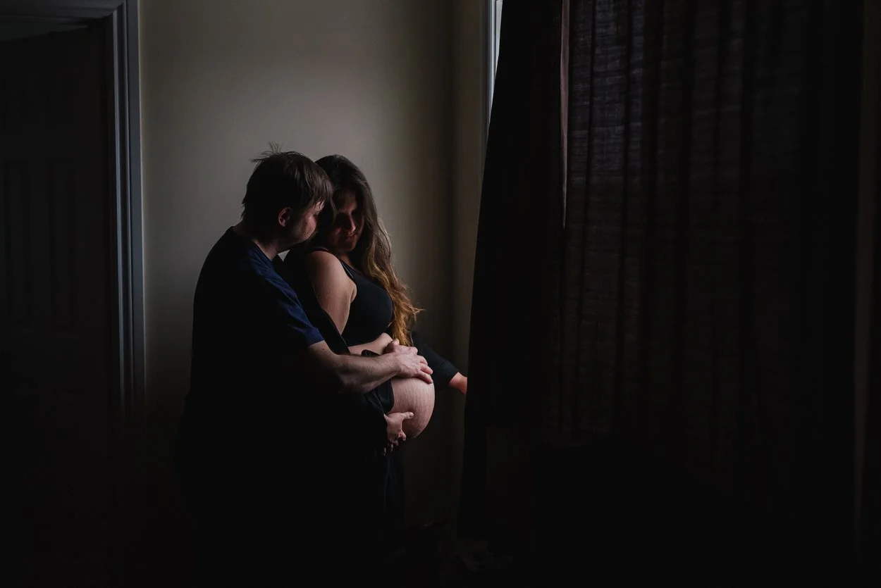 Man and woman standing in a slit of light during labour at home in Ottawa. The woman has long brown hair.
