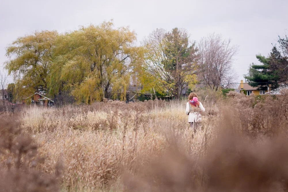 Mom and baby are walking through a huge garden by a willow tree in the fall at Kilborn Gardens in Elmvale Acres.