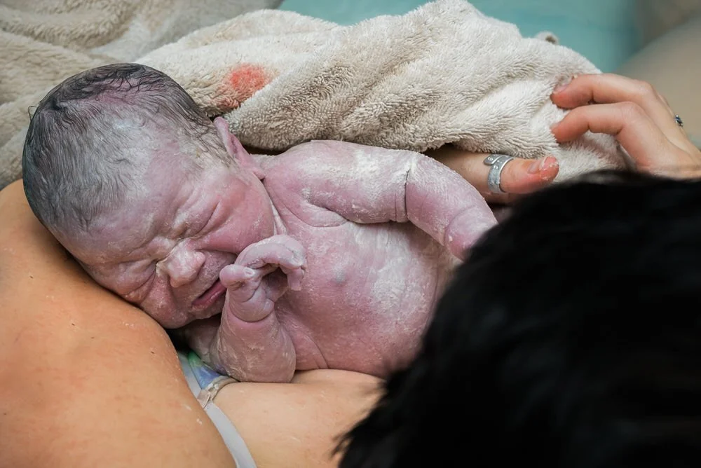 Newborn baby moments after birth in mom's arms covered in vermix wrapped in a towel.