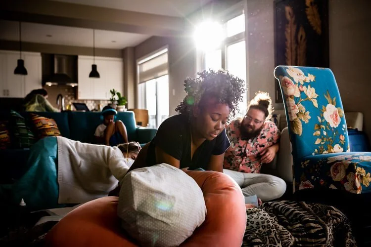 Mom in labour at home on the floor supported by family and her midwife. The sun is setting behind her.