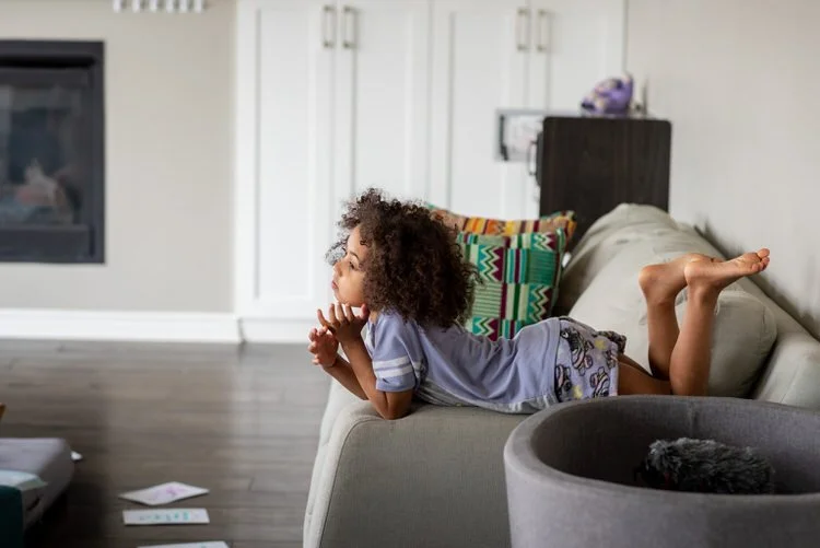 Big sister is siting on the couch overlooking her mom while her baby brother is being born during homebirth.