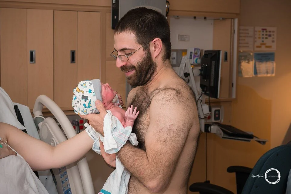 Dad holding his newborn daughter for the first time after birth, he is smiling and looking in her eyes.