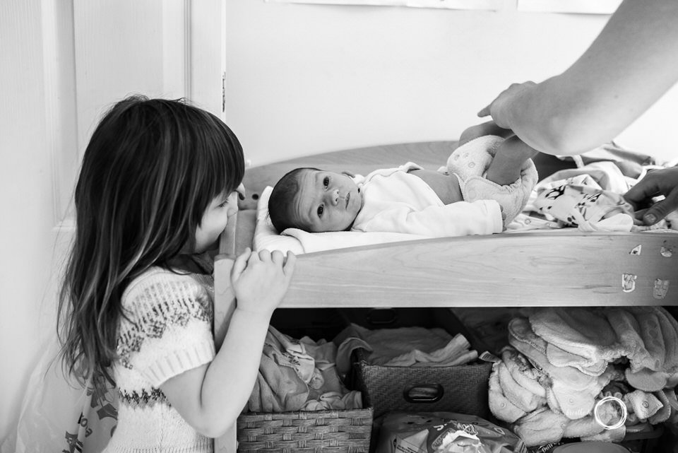 Big sister watches her newborn brother get his diaper changed.