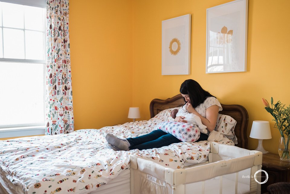 Mom breastfeeding new baby at home on bed in yellow room.