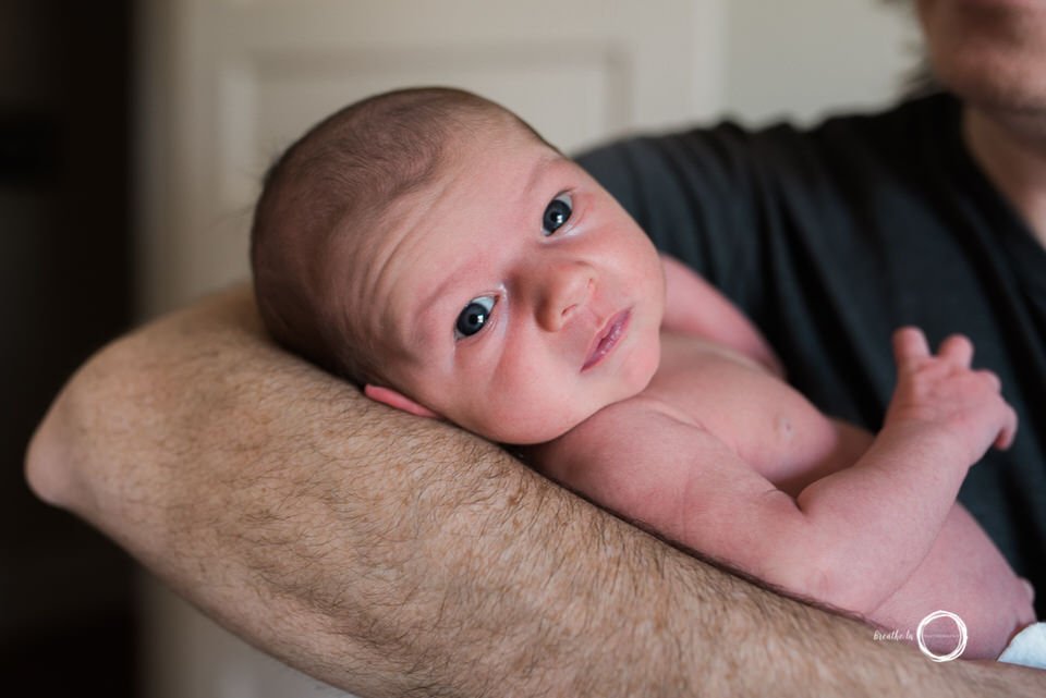 Newborn baby boy in dad's arms looking at camera.