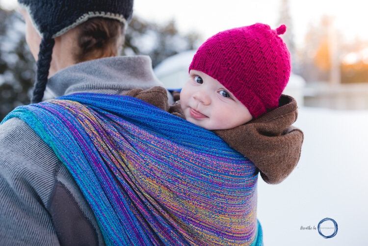 Baby with red hat smiling at the camera while on dad's back. The sun is setting behind them.