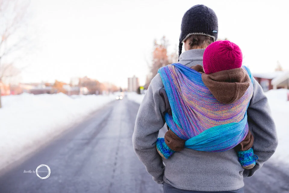 Dad and baby walking down the road in the winter. Baby is in red hat and wrapped in a beautiful blue and pink wrap.