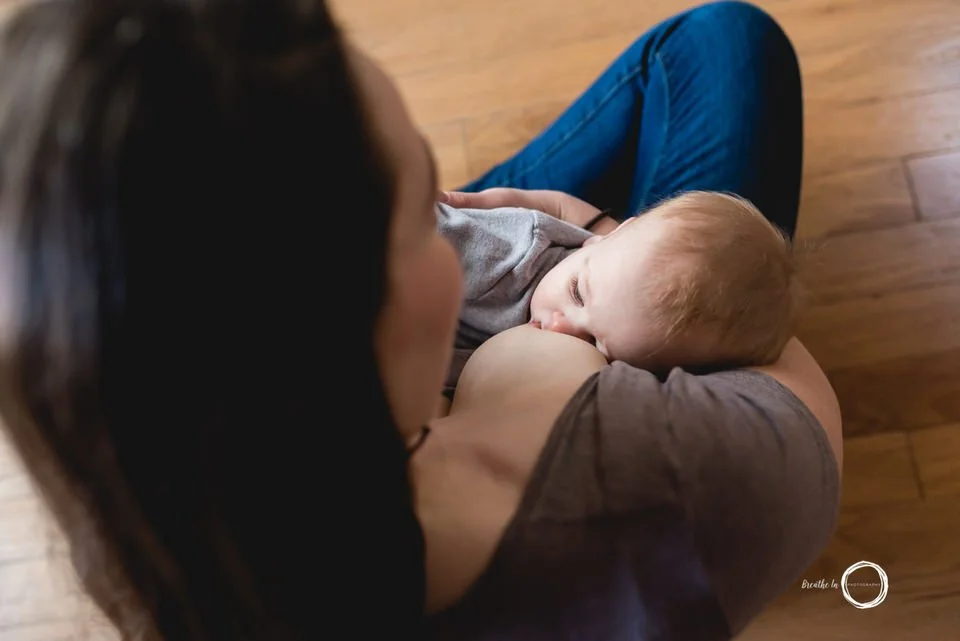Mom nursing her son while siting on the floor.