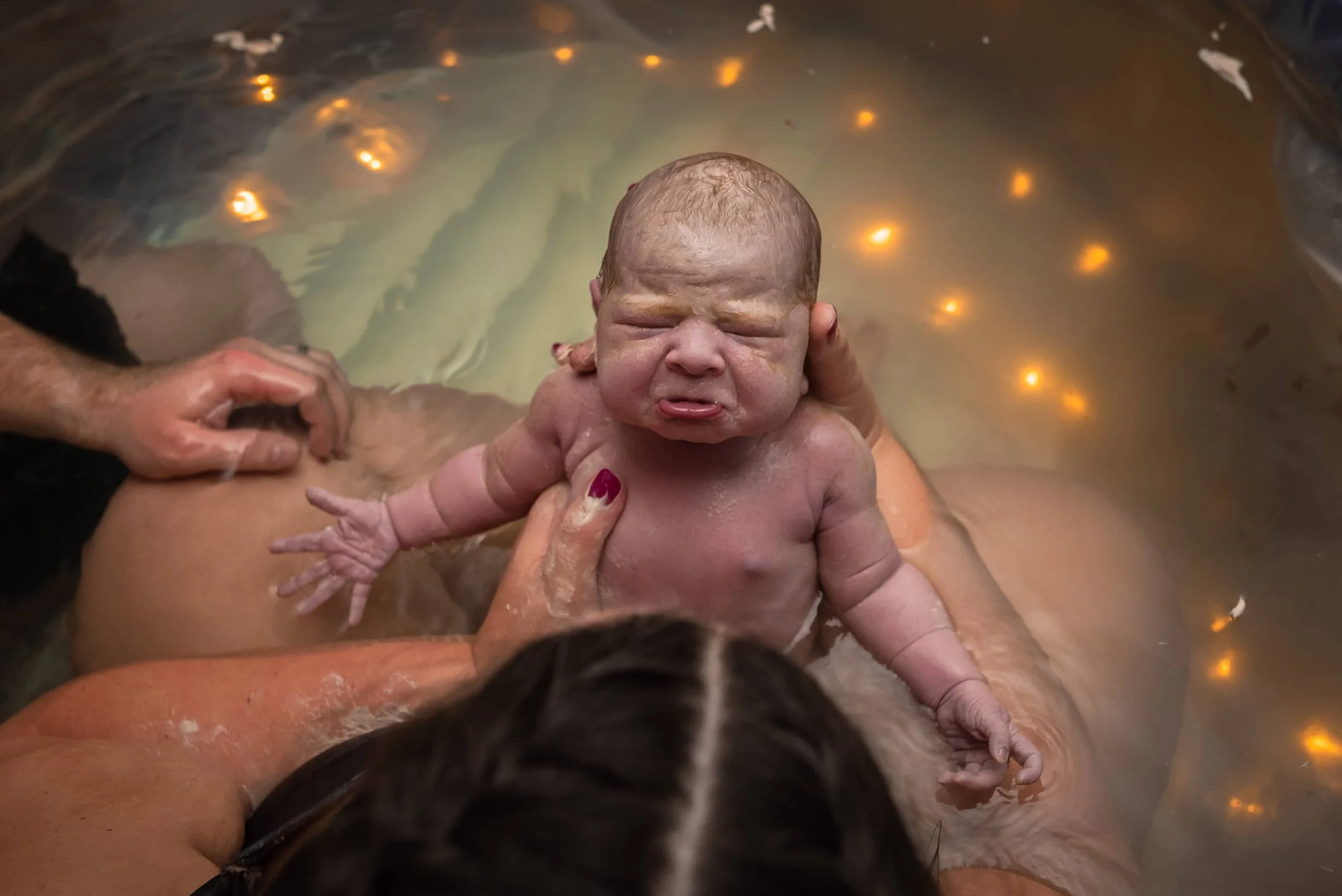 Newborn baby after water birth with a pouty adorable face in her mom's arms.