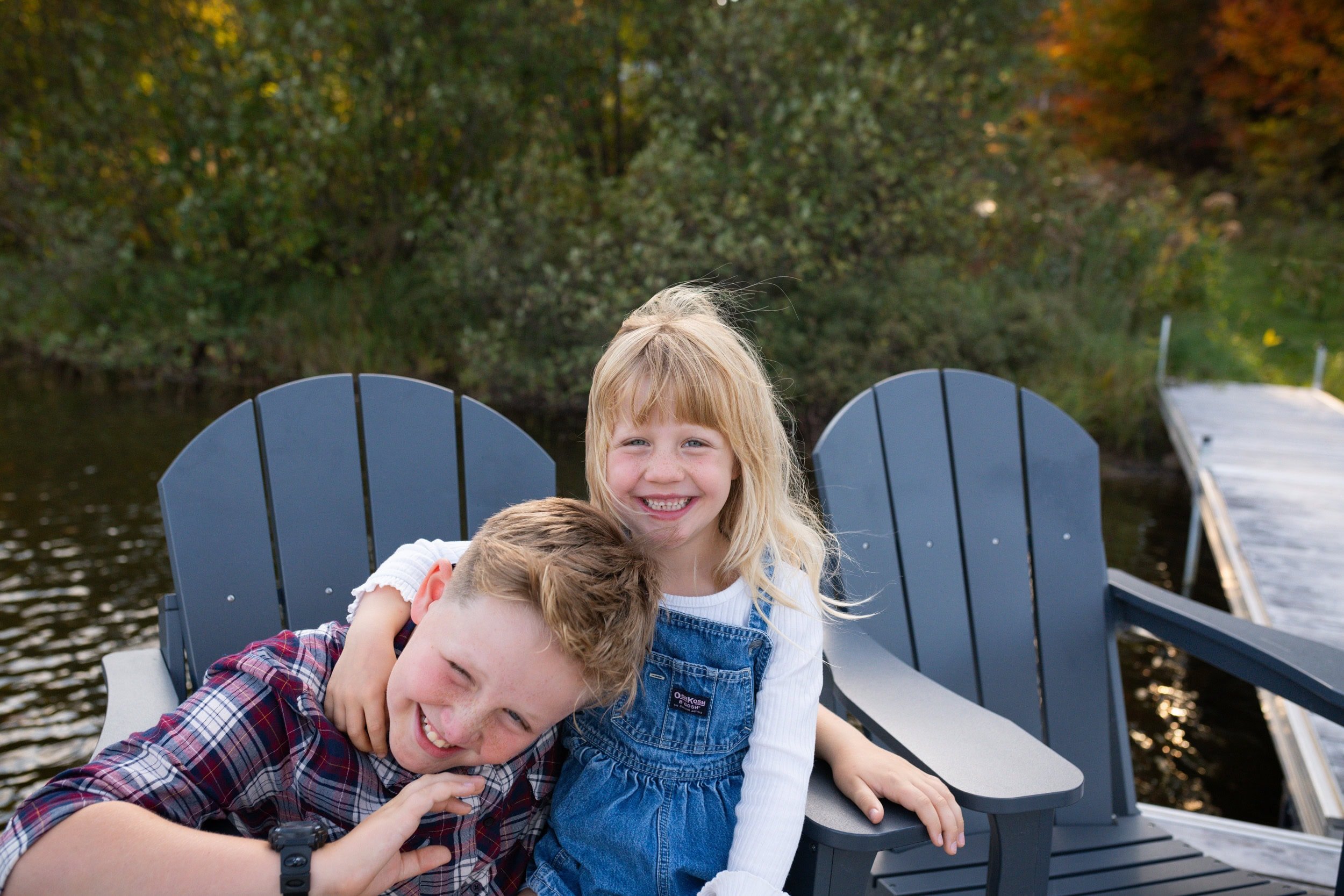 Brother and sister sitting on dock chairs with sunset behind them. They are laughing and having fun.