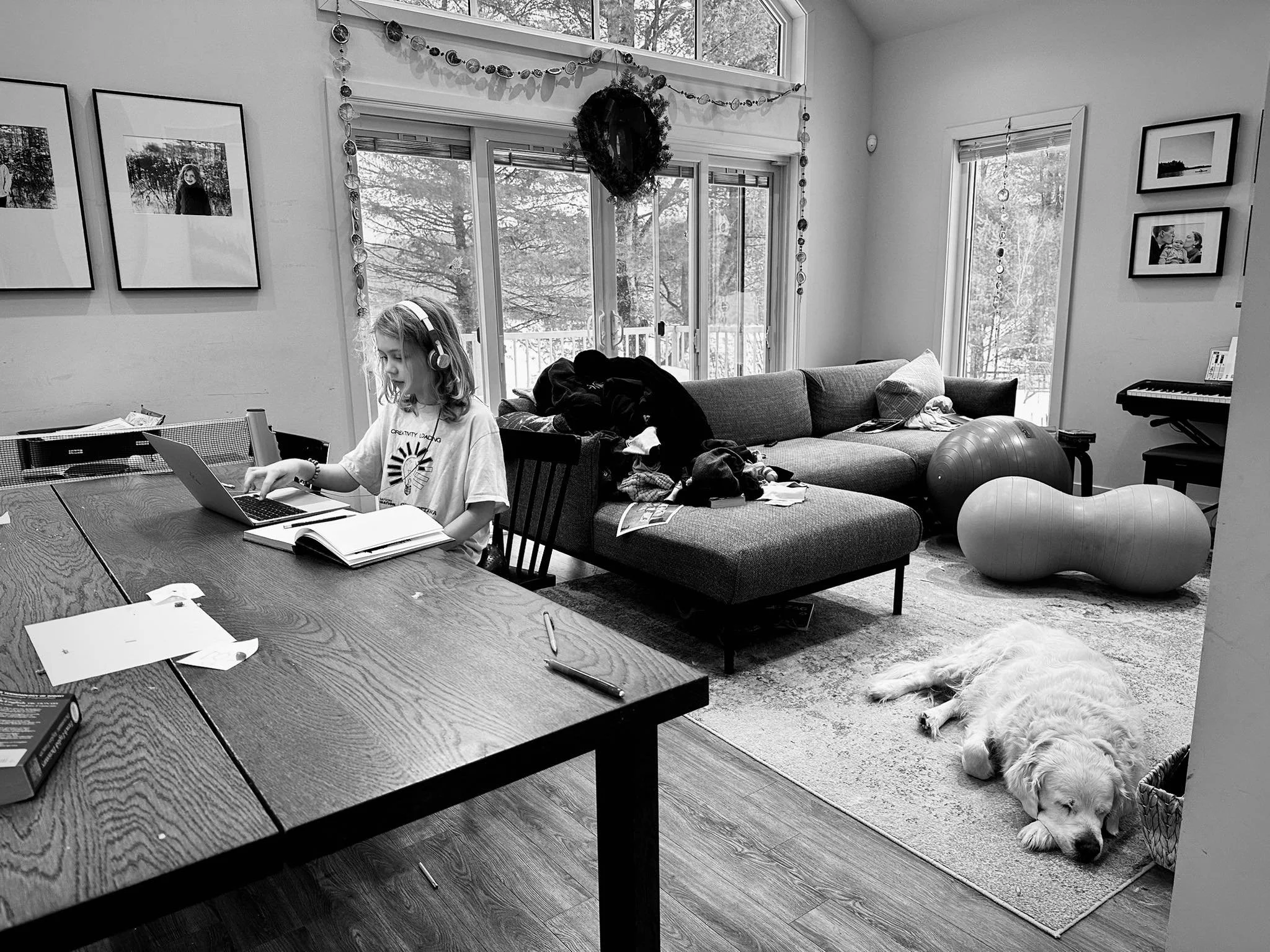 Boy sitting at table doing schoolwork surrounded by his home with family photos around him and a large sleeping dog.