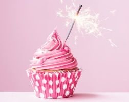 Eat a cupcake without guilt Pink cupcake with swirl frosting, a lit sparkler candle, and a pink polka dot cupcake liner against a pink background.