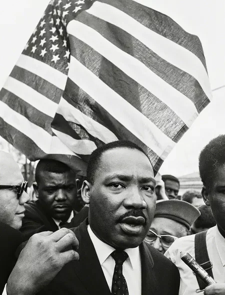 A black man in a suit and tie at a protest, holding an American flag on his shoulder, surrounded by other protesters.