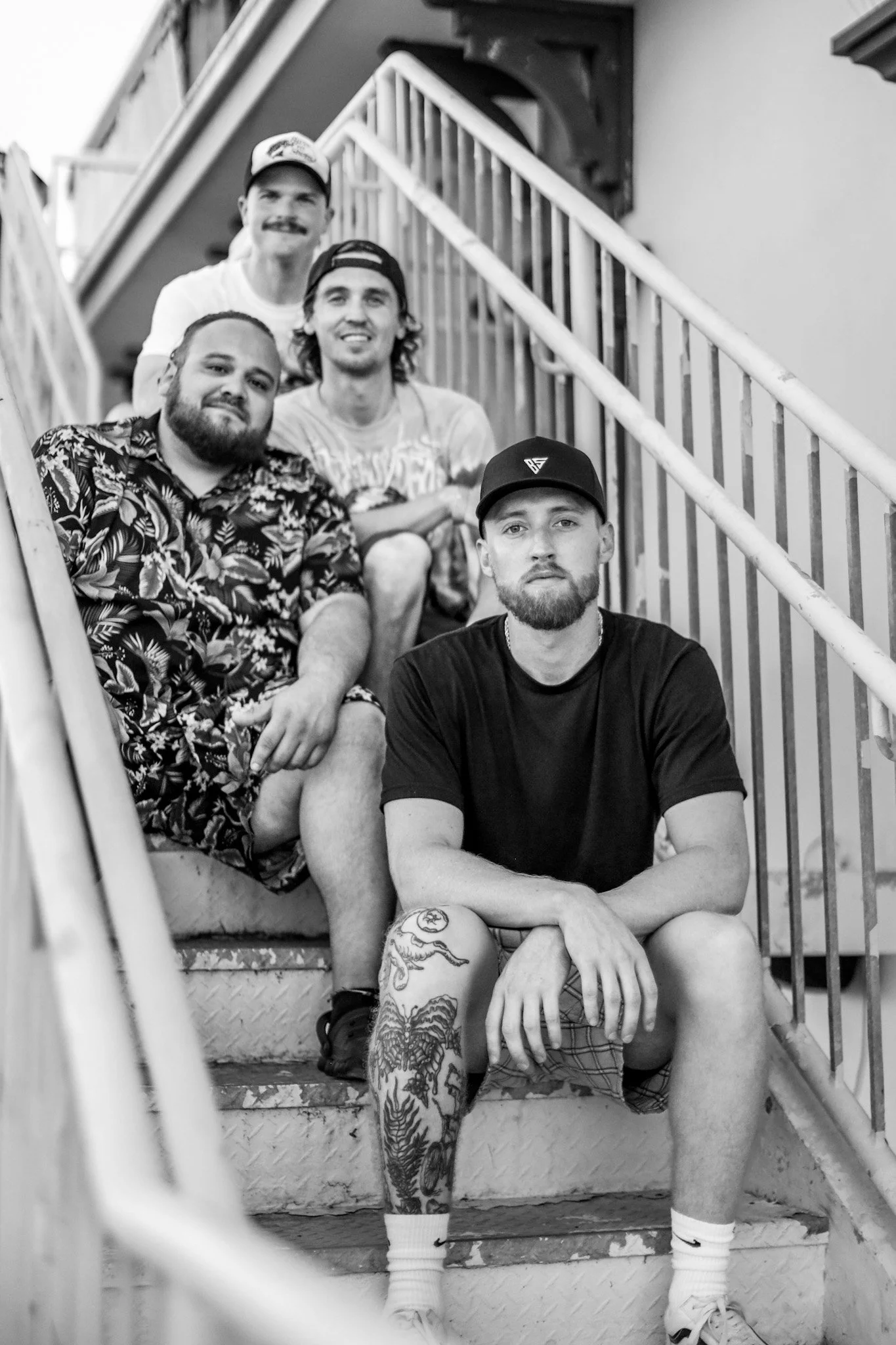 A black-and-white photo of five young men sitting on stairs outside a building, posing for the camera.