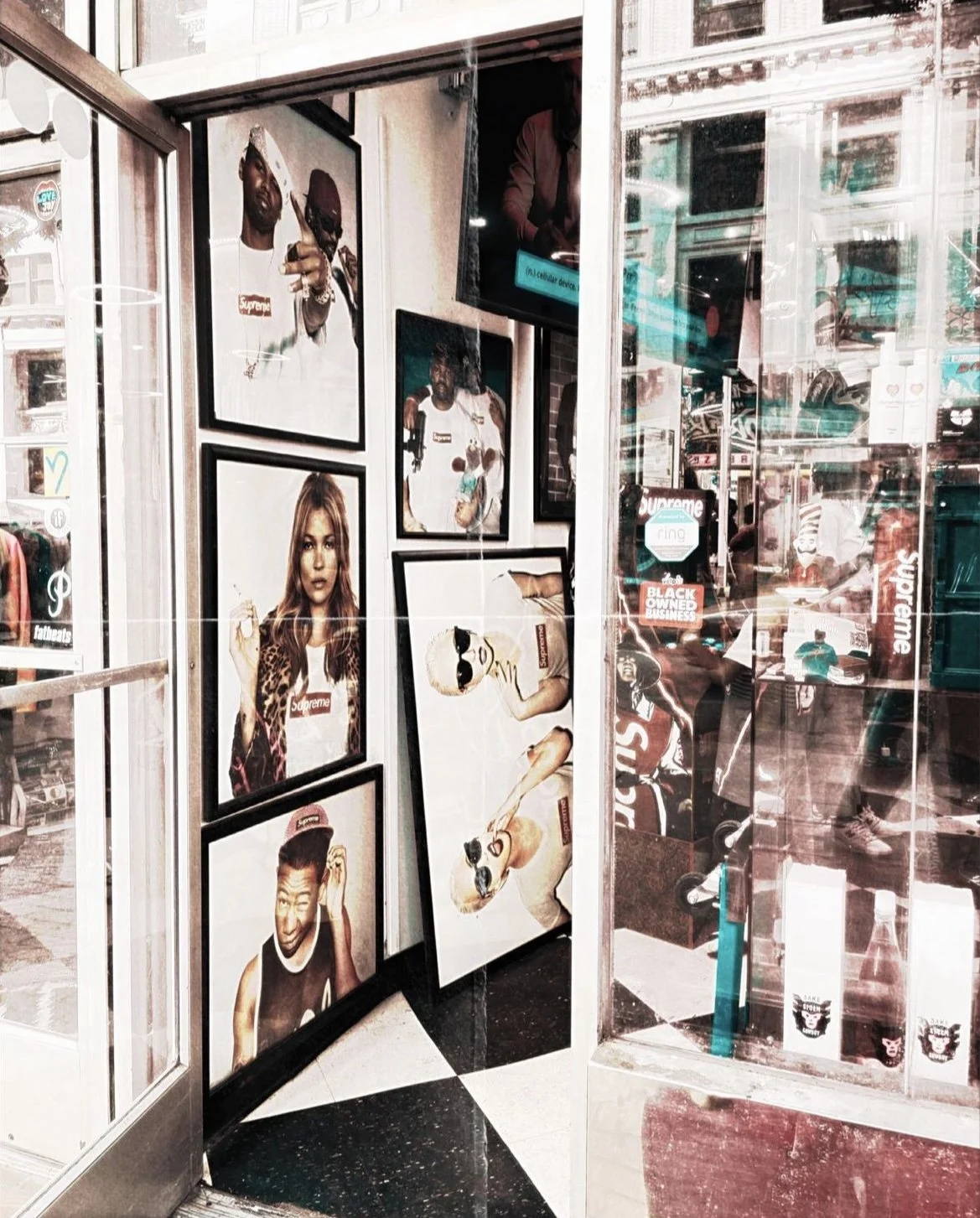 The image shows an interior of a store with framed photographs of diverse models and celebrities wearing Supreme-branded clothing on the wall.