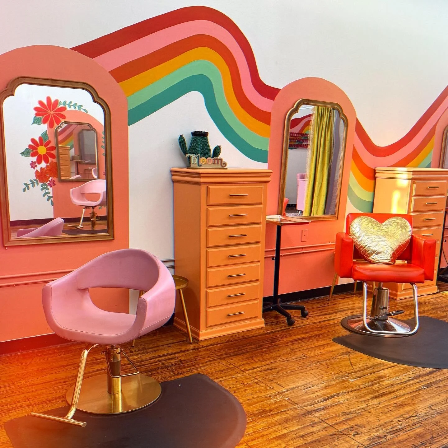 Colorful hair salon interior with pink chairs, wooden furniture, large mirrors, a rainbow mural, and cheerful decor.