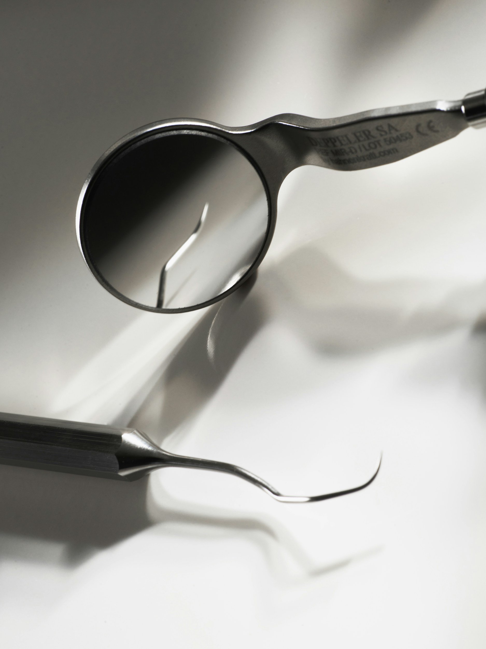 Close-up of dental tools, including a dental mirror and a dental pick, on a white surface.