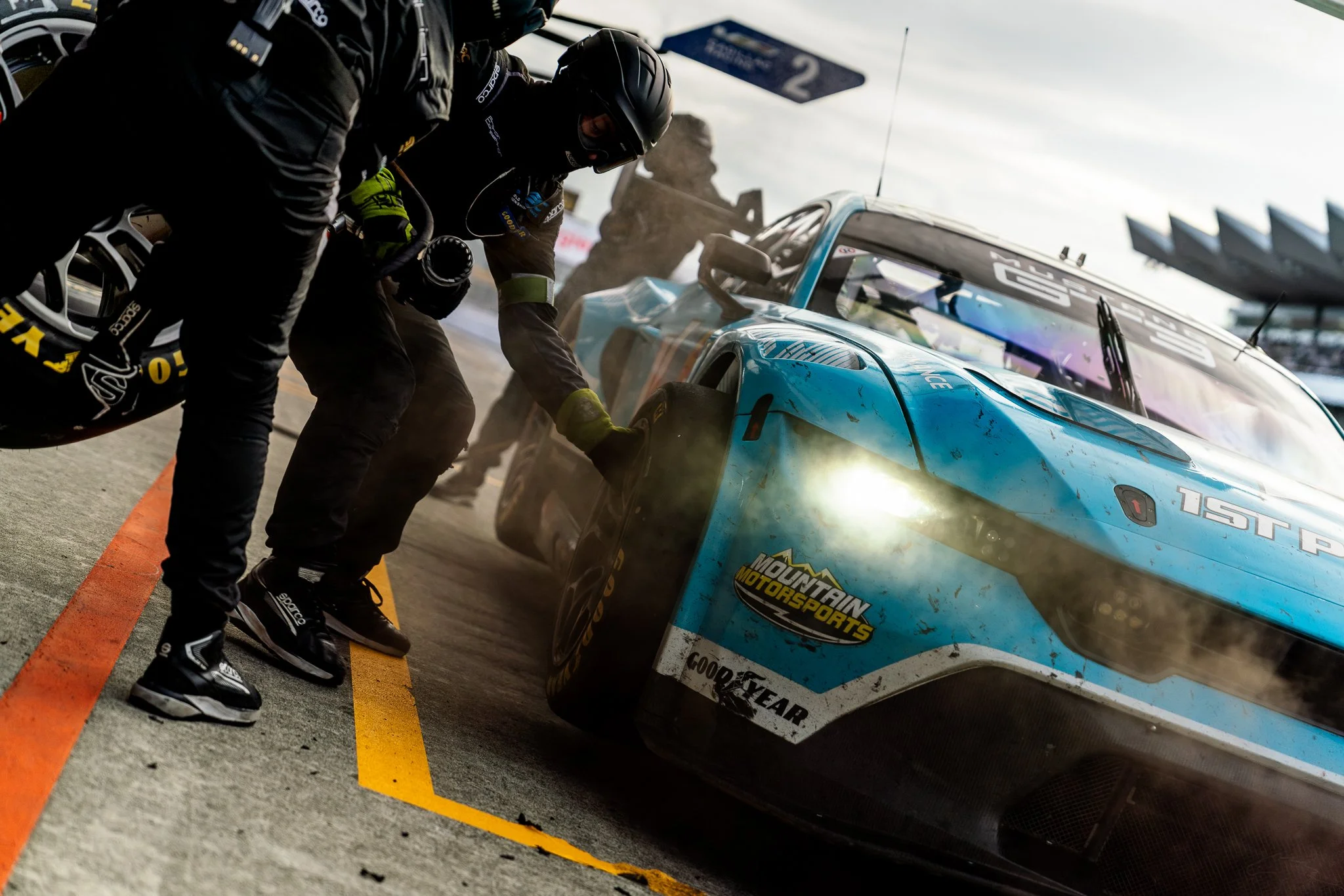Mustang GT3 race car being serviced by pit crew, with a mechanic pulling a tyre off as brake dust sprays during the 2024 World Endurance Championship race at Fuji Speedway, Japan.