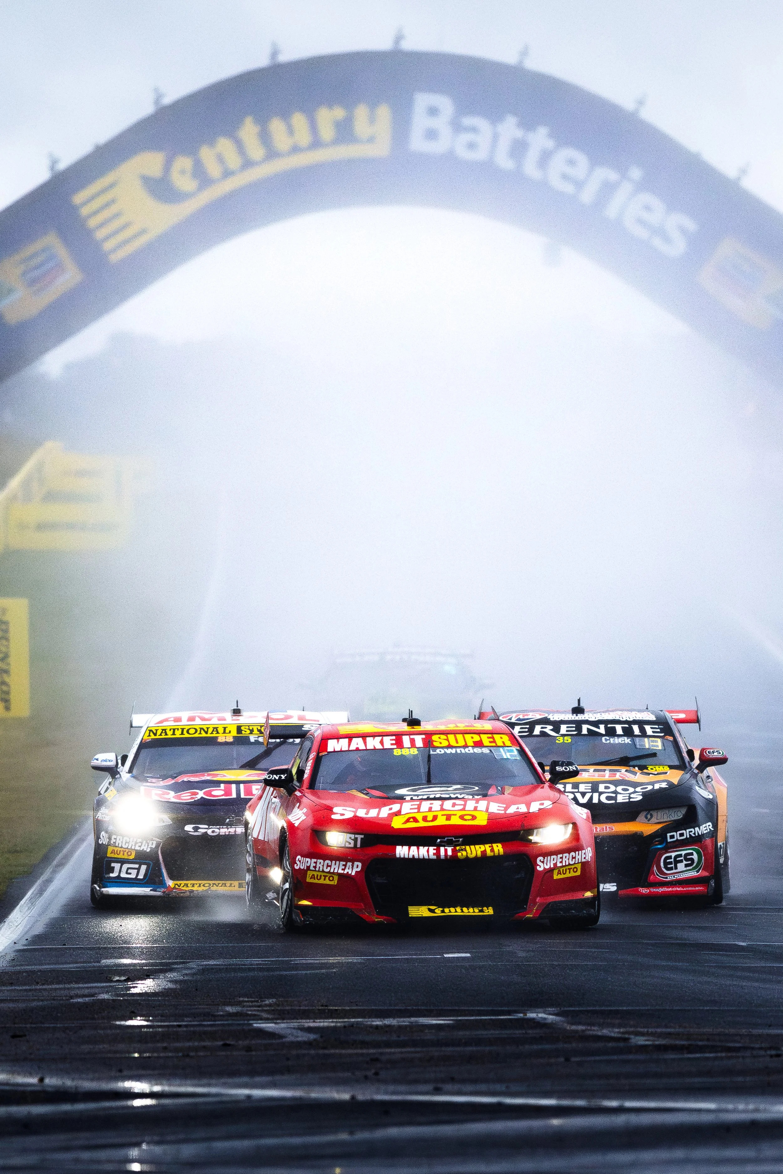 A group of Supercars led by Triple Eight Race Engineering’s Camaro ZL1 driven by Craig Lowndes and Zach Bates, with spray from the cars behind.