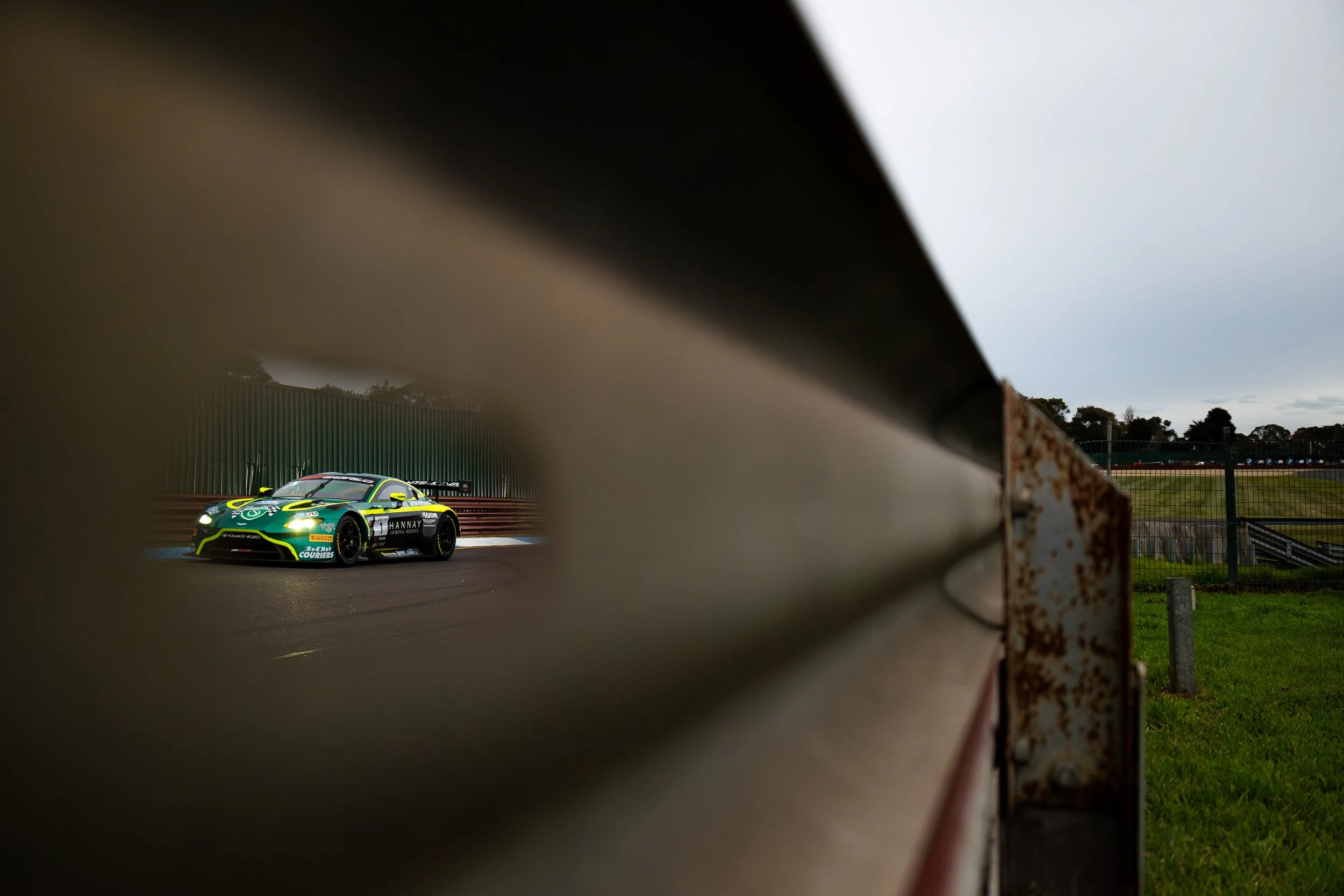 Race car Volonte Rosso Sandown Raceway 2025 captured through a barrier hole. 