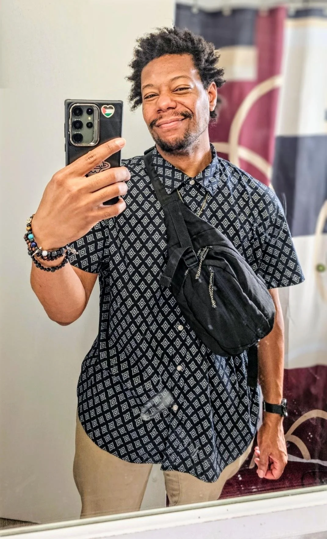 Dre, a light-skinned enby with black free form locks in a patterned black button-up 