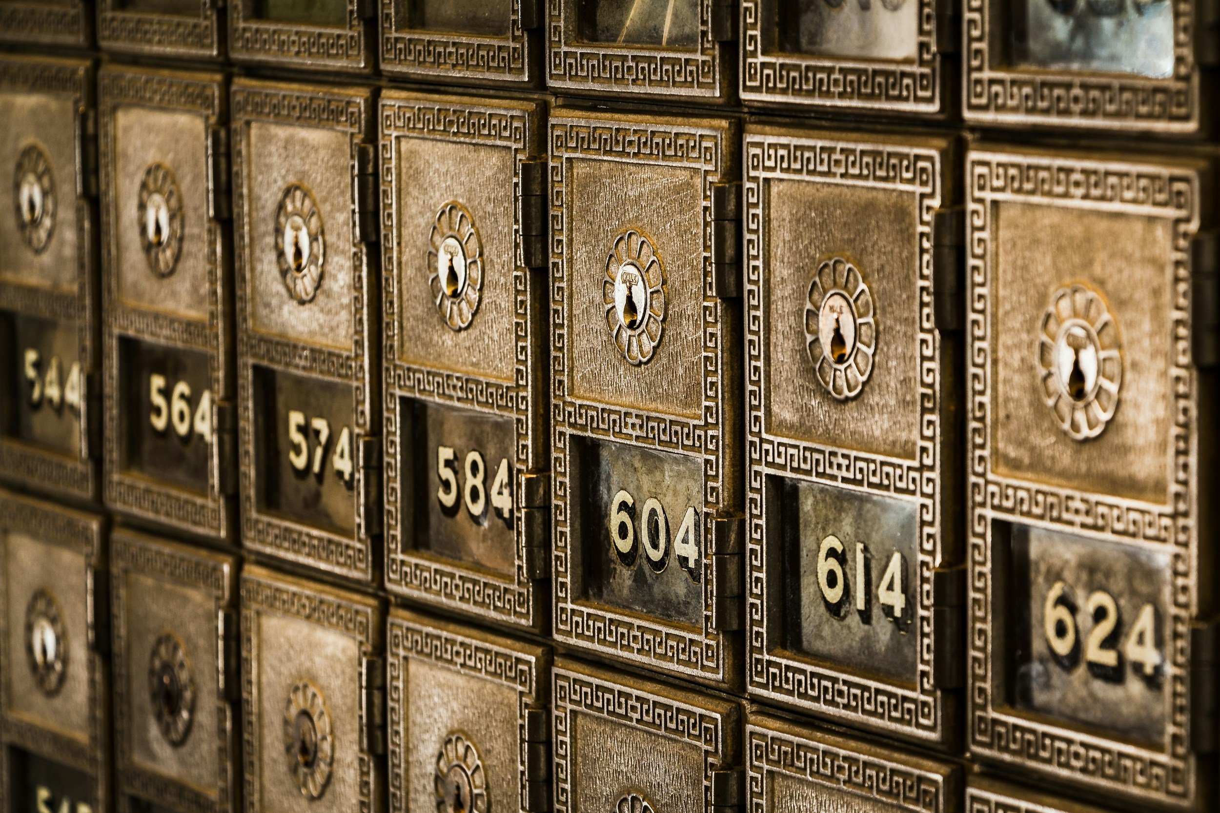 Close-up of vintage metal mailboxes with number labels, arranged in a grid, with decorative borders and keyholes.