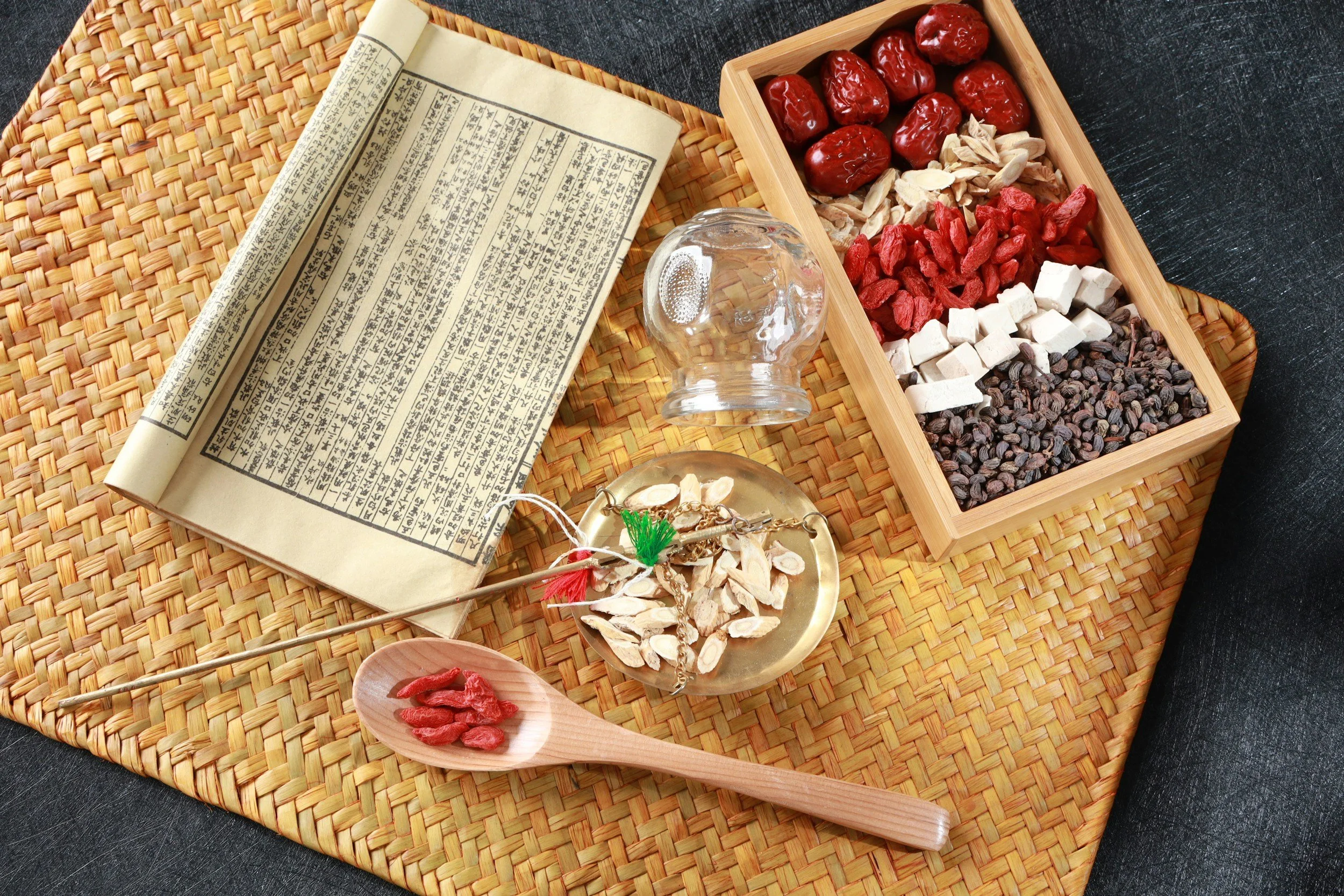 Traditional Chinese medicine ingredients and text on paper, including dried herbs, roots, seeds, and grains on a woven mat.