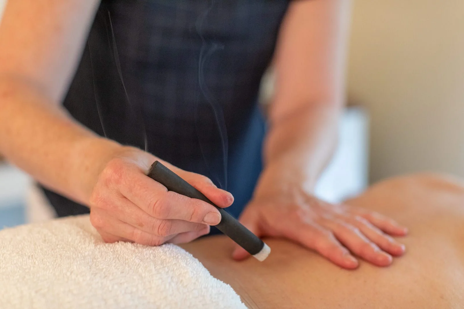 Close-up of a person receiving a massage, with a massage stick in their hand and applying pressure to their back.