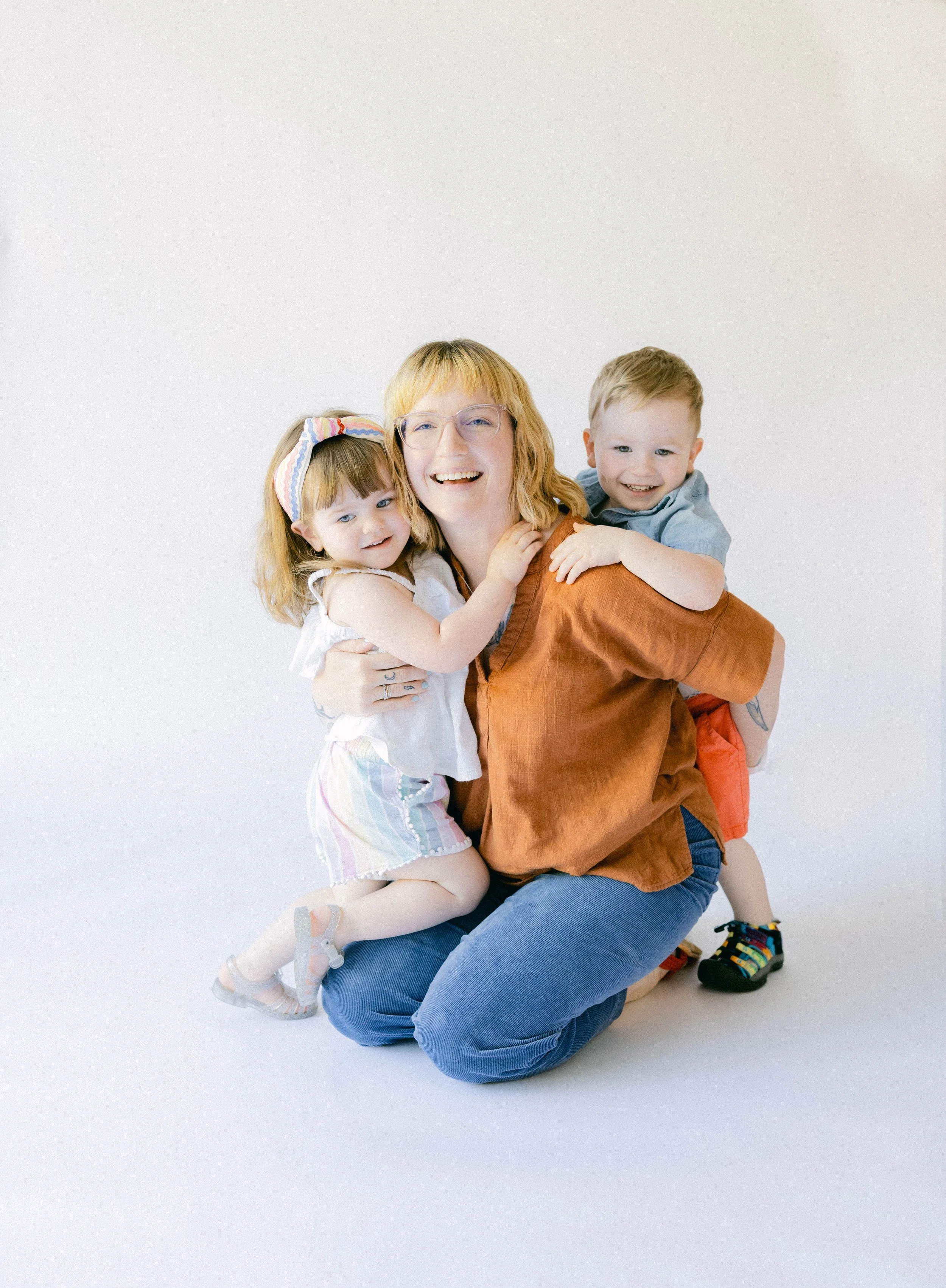 Emily is kneeling on the floor being hugged by her two children