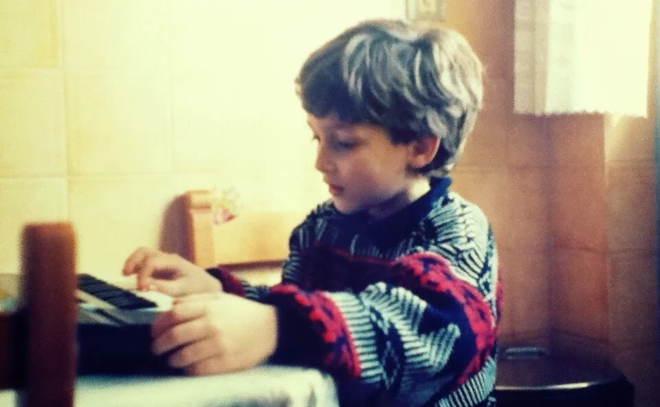 A young boy with curly hair playing a keyboard at a table.