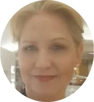 Close-up of a woman's face with light makeup and blonde hair, smiling slightly.