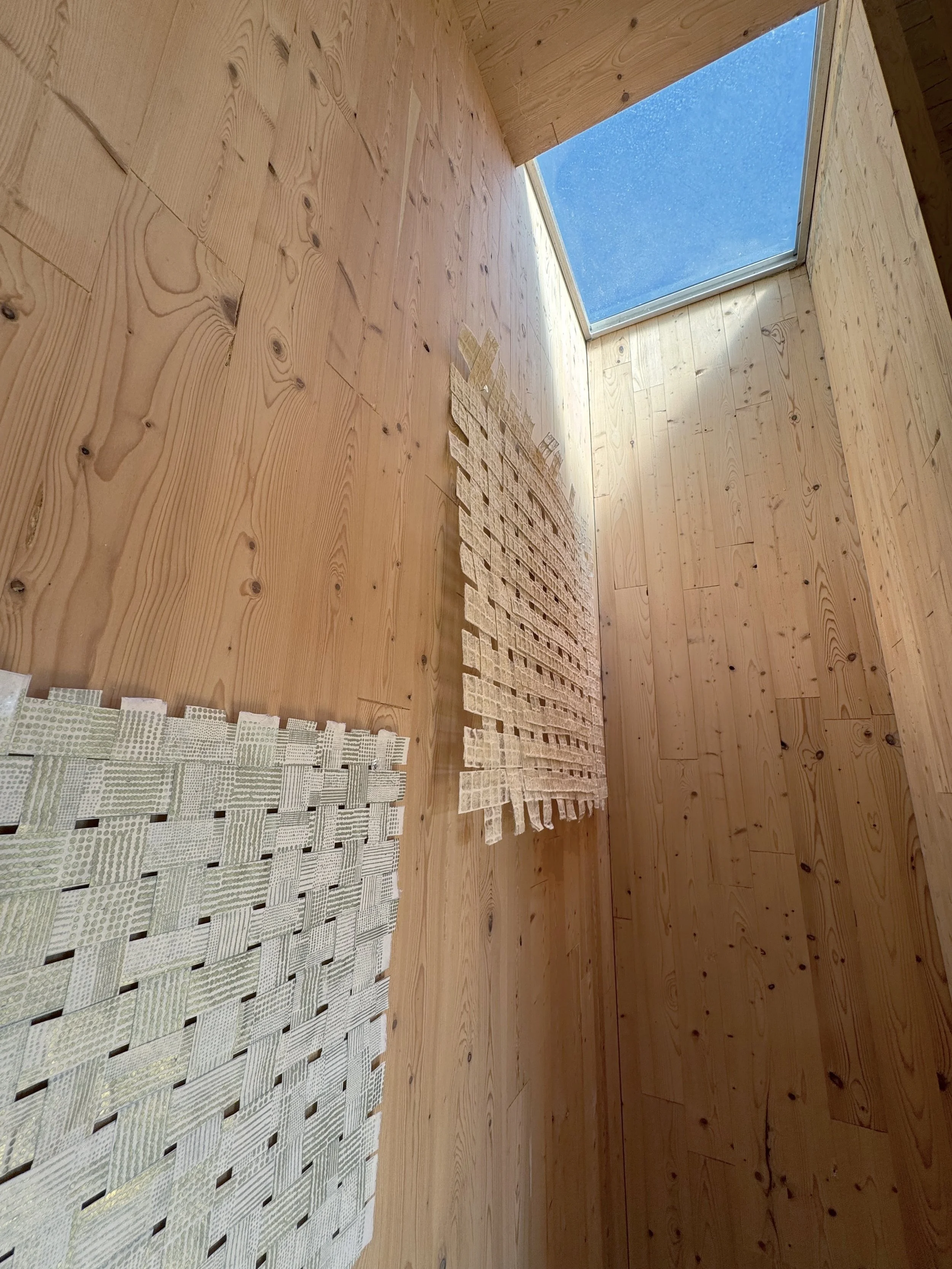 Interior of a wooden room with a skylight, wooden walls, and woven wall hangings.