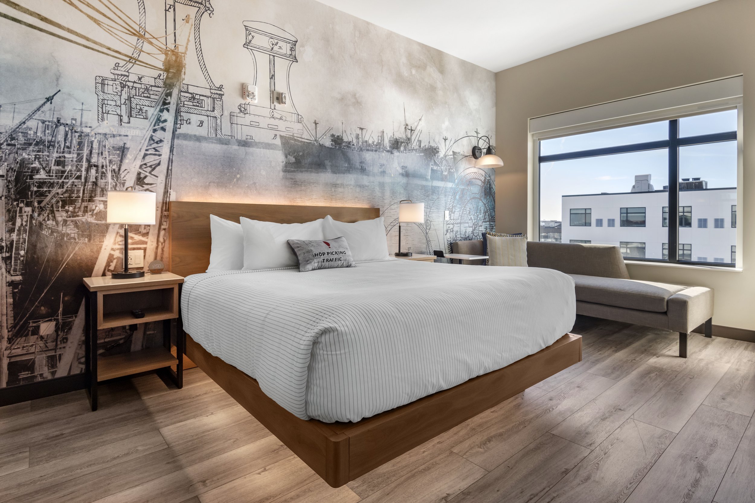 Modern spacious lobby with light gray sofas, large windows with dark curtains, a glass coffee table, a round glass table with a white orchid plant, a stylish chandelier, and decorative wall art.