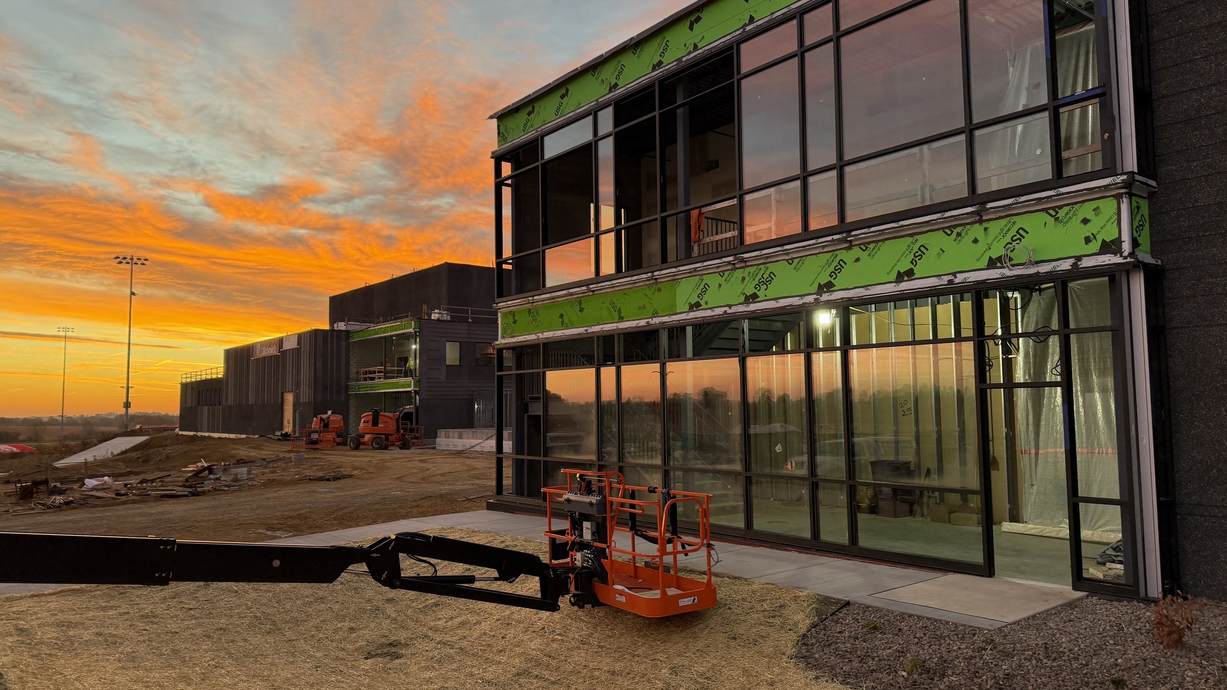Image of Monroe Highschool under construction. The big walls of glass windows are in the front. The sun is setting in the background.