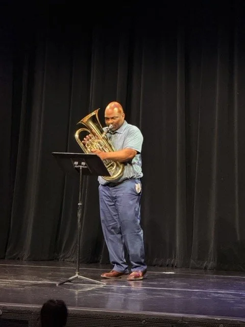 A man playing a euphonium on a stage with black curtains behind him.