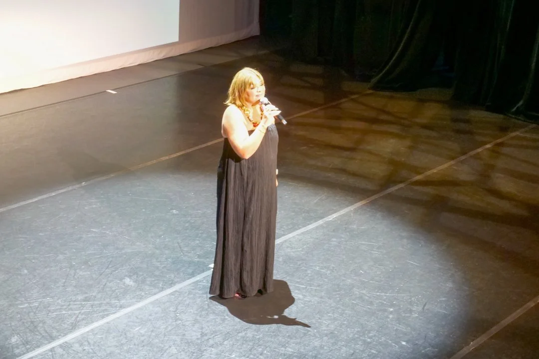 A woman in a black dress performing on stage with a microphone.